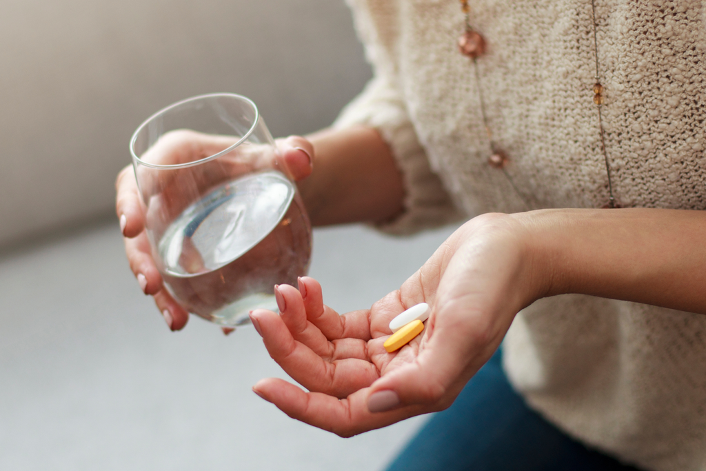 A woman holding vitamins and a glass of water